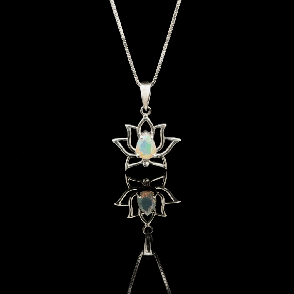 Ethiopian Opal Lotus Pendant, a sterling silver creation featuring a lotus flower design with an Ethiopian opal at its center, elegantly hangs on a delicate chain and is displayed against a reflective black surface.