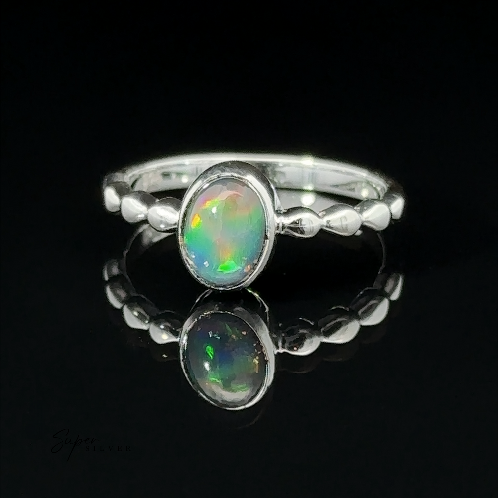 
                  
                    A Oval Gemstone Ring with Beaded Band with an oval opal set in the center, displayed on a reflective black surface showing its reflection.
                  
                