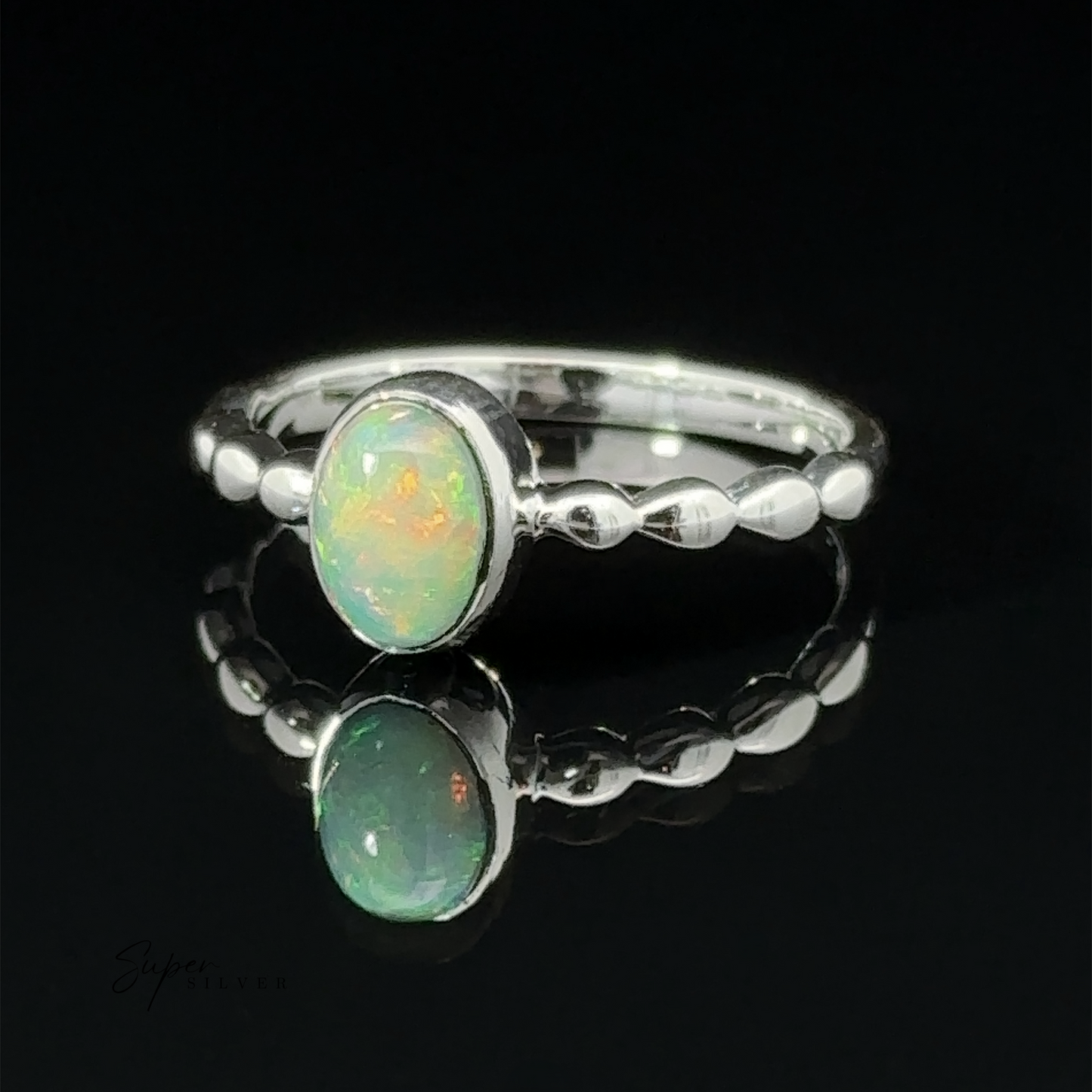
                  
                    Oval Gemstone Ring with Beaded Band with an oval opal stone, displayed on a reflective surface against a dark background.
                  
                
