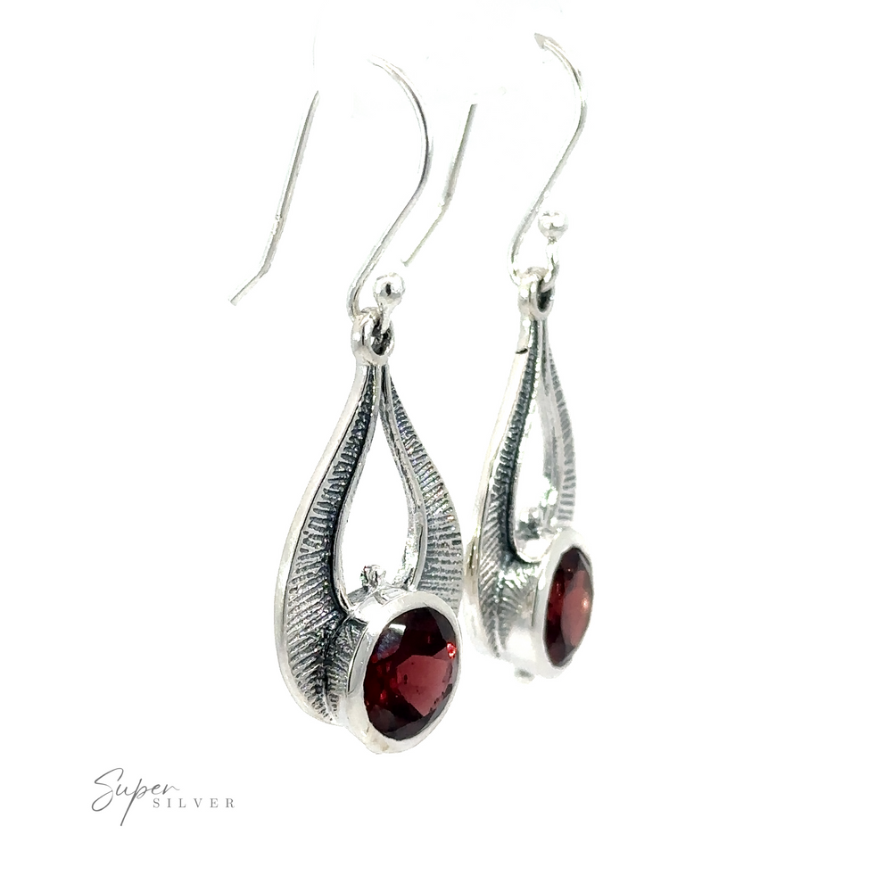 
                  
                    Winged Gemstone Earrings featuring elongated, teardrop-shaped settings with dark red garnet gemstones at the center. The brand name "Super Silver" is visible in the bottom left corner.
                  
                