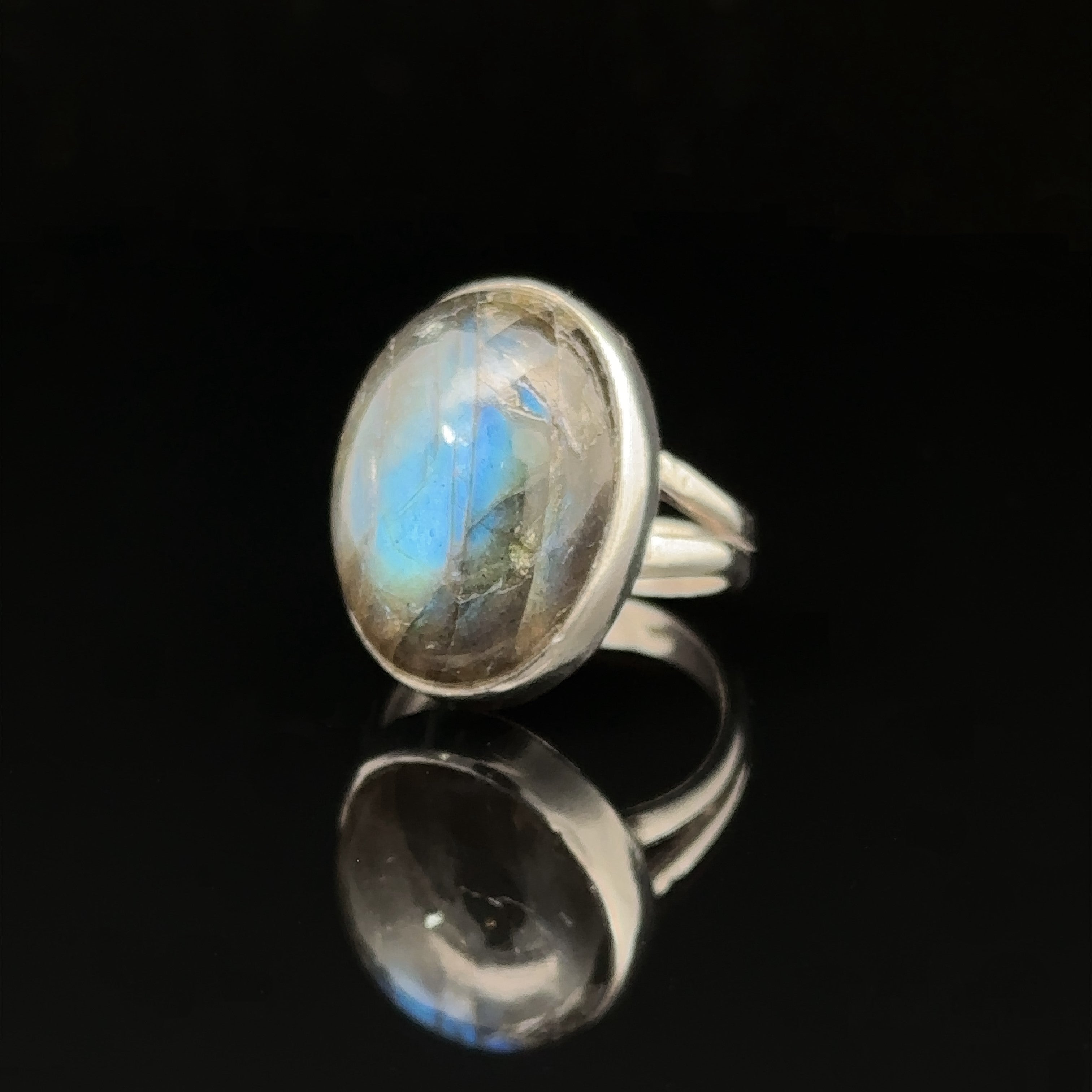 An heavy oval Labradorite ring with a sterling silver band displayed on a reflective black surface.