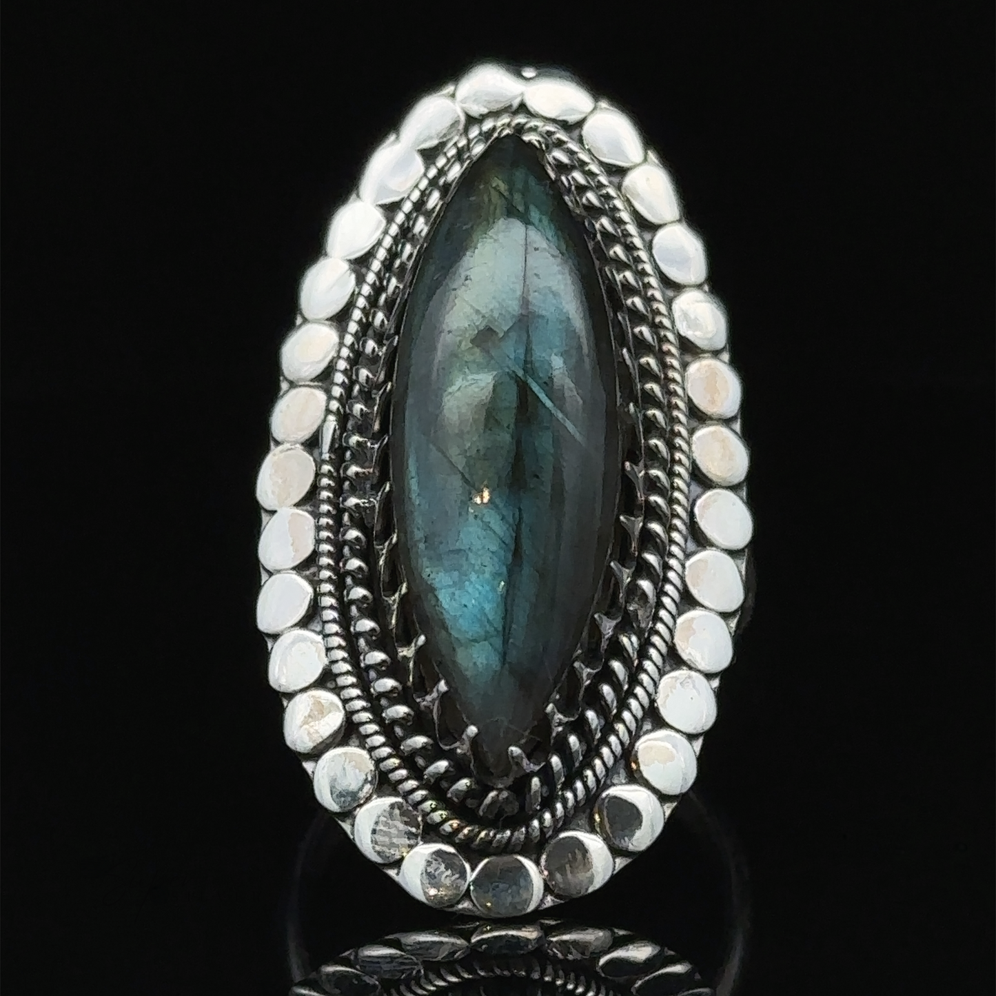 
                  
                    A Statement Marquise Shaped Gemstone Ring with a large, oval-shaped blue-green gemstone, surrounded by intricate detailing and small silver beads, embodies the essence of bohemian jewelry. Set against a black background, this piece is truly eye-catching.
                  
                