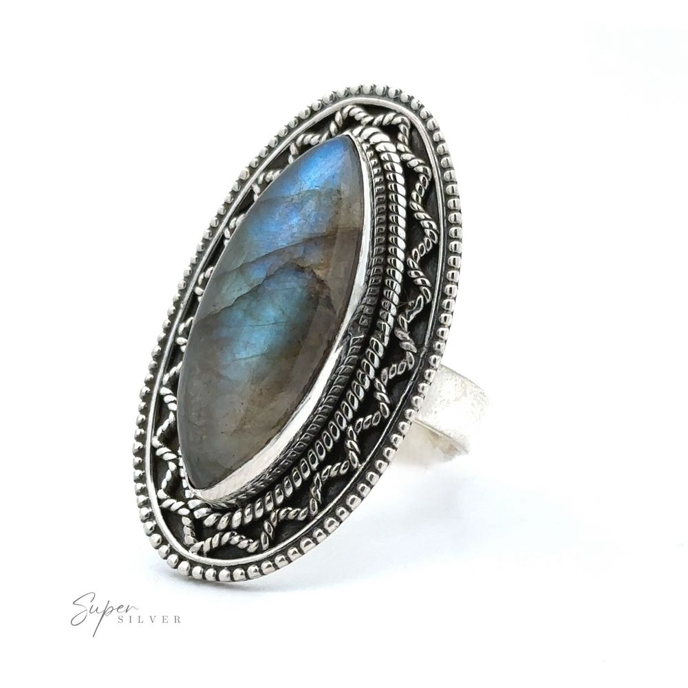 
                  
                    An intricately designed Marquise Shaped Gemstone Ring With Vintage Shield Border featuring an oval labradorite stone with blue and green hues, set within ornate silver detailing. With a bohemian twist and vintage appeal, this piece exudes charm. The "Super Silver" logo is visible in the bottom left corner.
                  
                