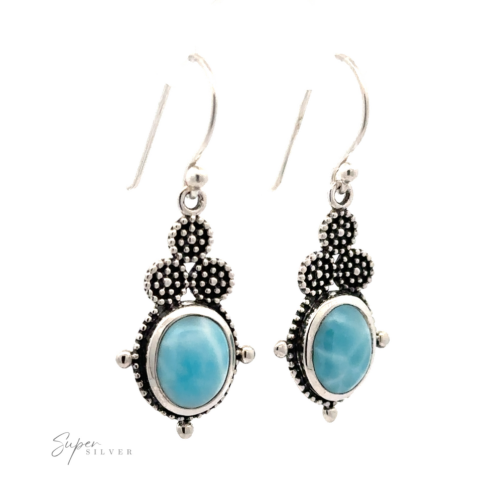 Super Silver offers a pair of Beaded Oval Larimar Dangle Earrings featuring oval-shaped blue Larimar stones and an intricate beaded design above the stones.