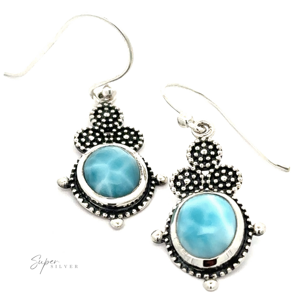A pair of sterling silver earrings with blue oval gemstones and a beaded design. The elegant design is complemented by hook attachments, showcasing the charm of Beaded Oval Larimar Dangle Earrings.