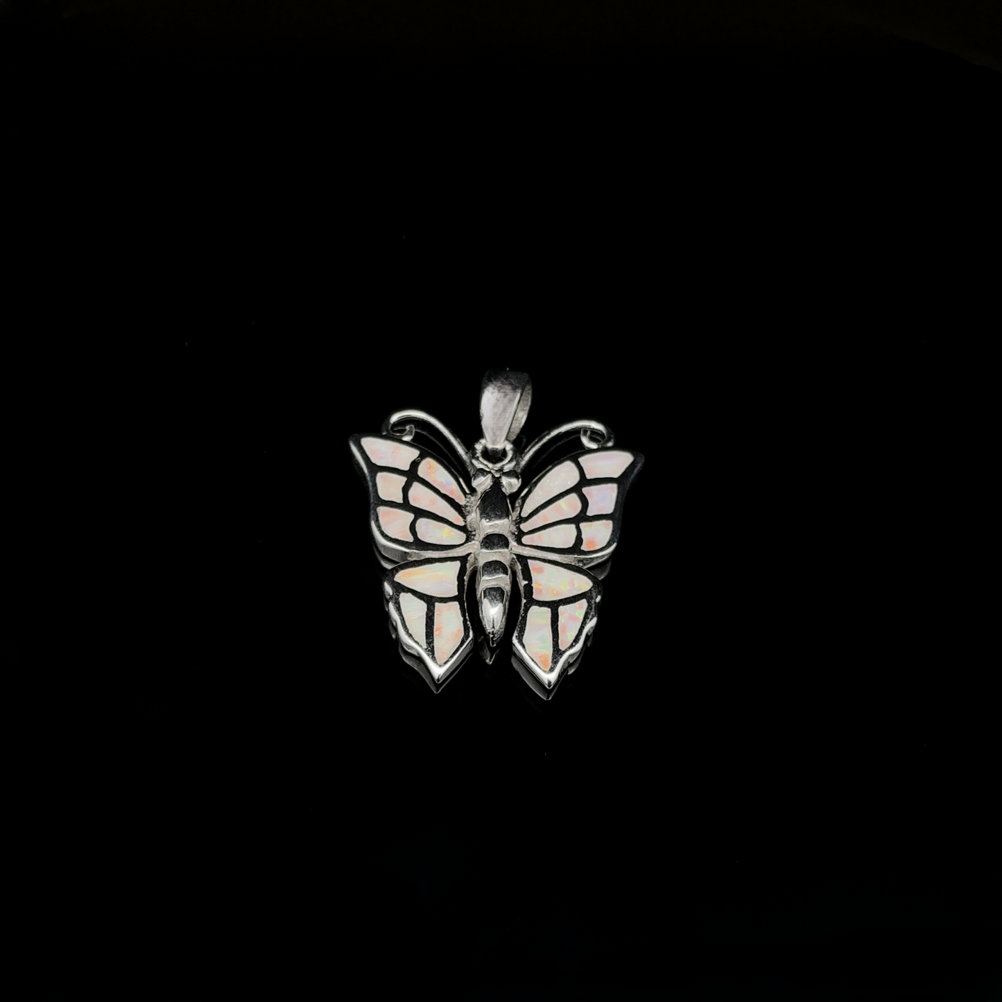 
                  
                    The Lab-Created Opal Butterfly Pendant features a stunning sterling silver design with wings resembling stained glass, set against a black background.
                  
                