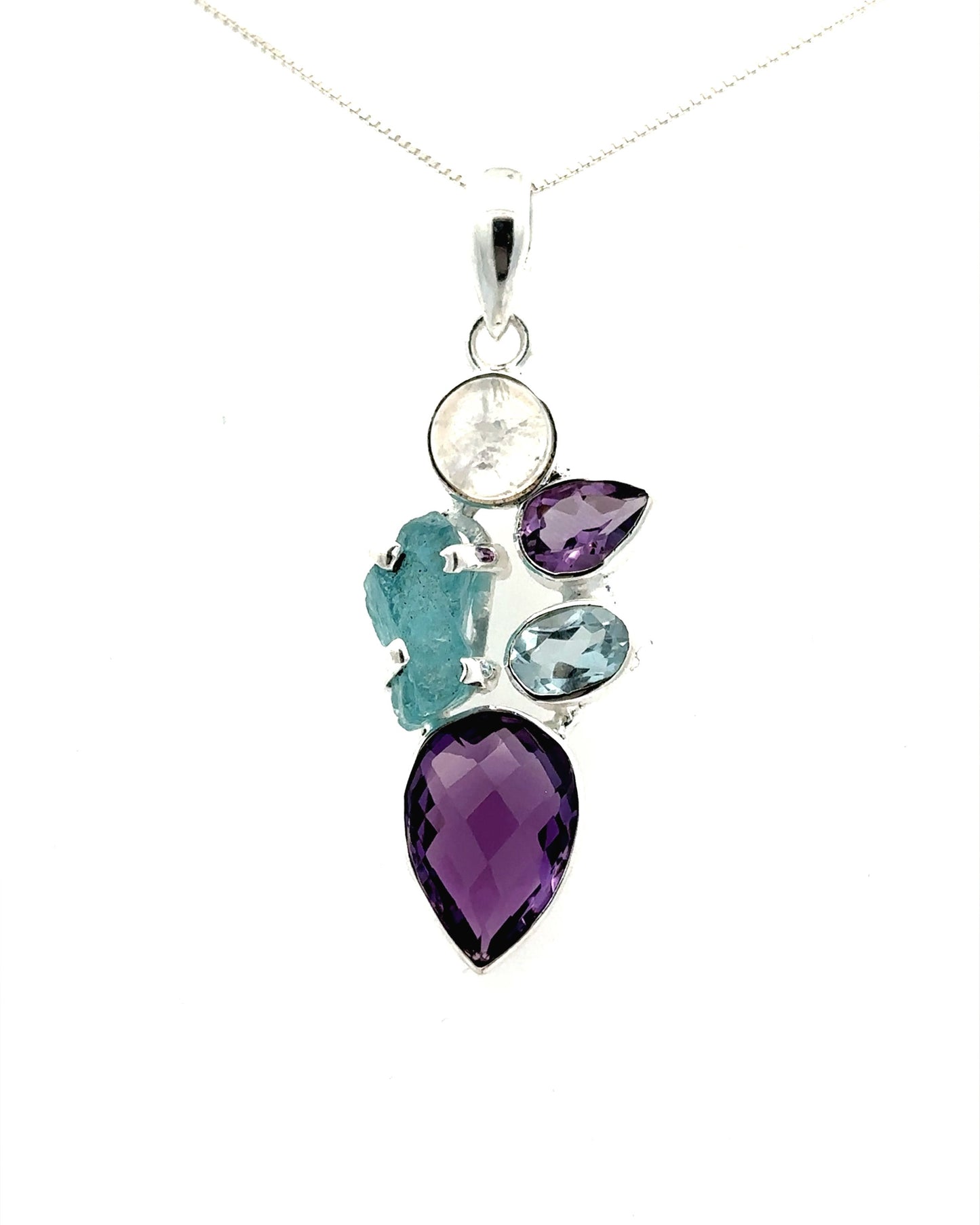 The Amethyst Multi Stone Pendant, featuring five gemstones in an array of shapes and colors—purple amethyst, teal, clear, and blue—is elegantly set in a silver mount that exemplifies bohemian jewelry as it hangs gracefully on a chain.