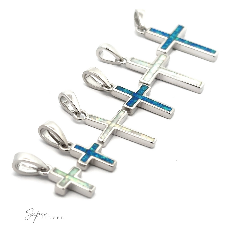 
                  
                    A row of five Lab-Created Opal Cross Pendants, crafted from sterling silver and featuring minimalist designs with striking blue and green opal inlays, is displayed on a white background.
                  
                