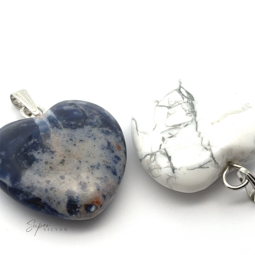 
                  
                    Two **Heart Stone Pendants** lay on a white surface. One is blue with speckles, and the other is white with grey vein-like patterns. Both feature metal loops for attaching to a chain or string, making them perfect for everyday wear.
                  
                