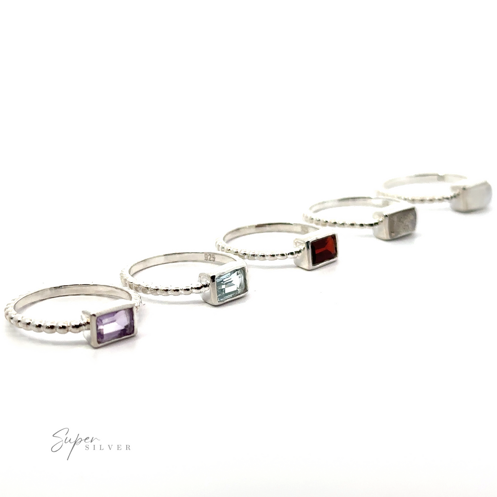 Five Rectangular Gemstone Rings with Beaded Bands, including Amethyst, arranged in a line against a white background.