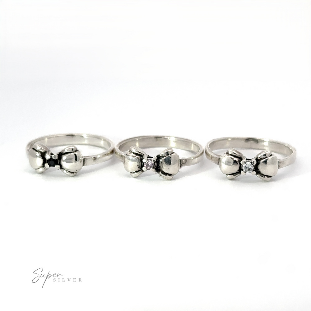 Three Adorable Cubic Zirconia Bow Rings with bow-shaped designs and small central gemstones are lined up against a white background. One features a striking black cubic zirconia. The text 