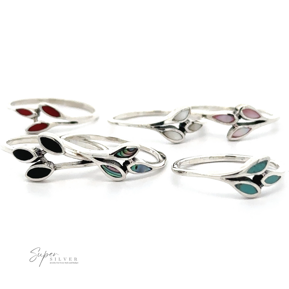 A collection of sterling silver rings, including Tiny Leaves Ring with Inlaid Stones and other minimalist styles, with various colored gem accents arranged on a white background. Super Silver branding is visible in the bottom left corner.