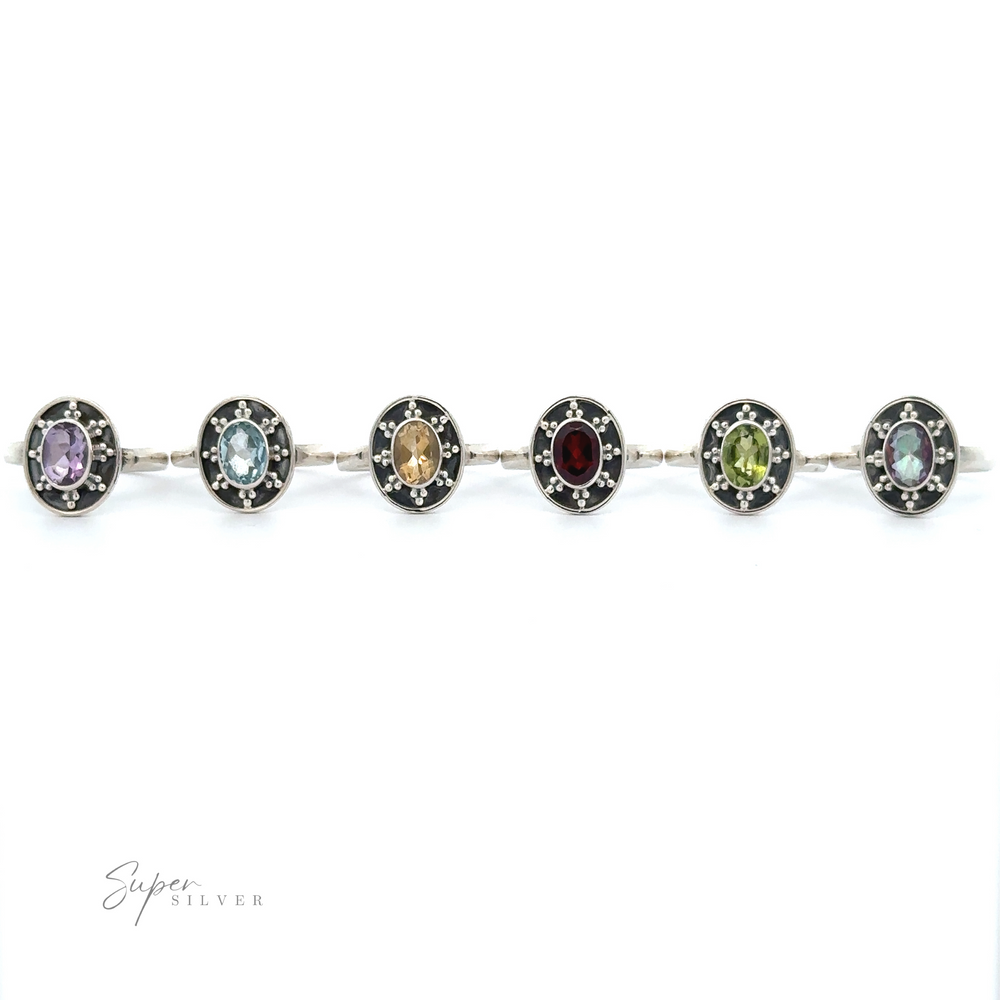 A silver bracelet with six round gemstone charms is displayed. Reminiscent of vintage-inspired jewelry, the gemstones dazzle in varied colors: purple, blue, yellow, red, blue-green, and green.