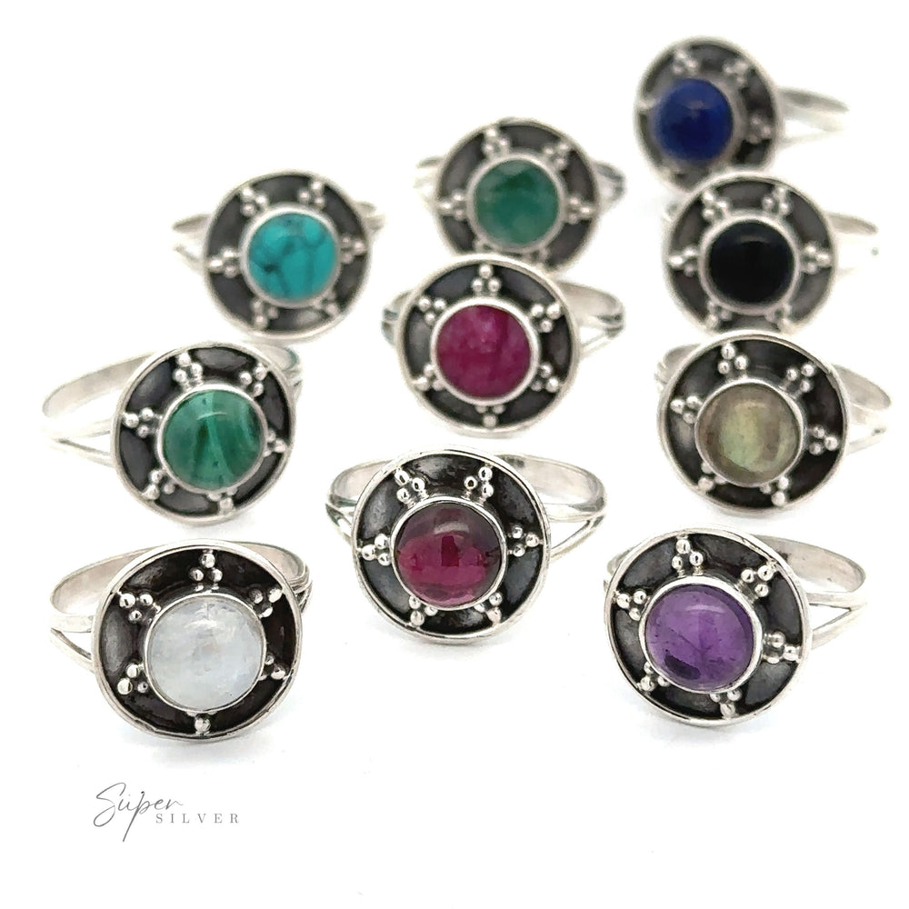 A collection of nine Gemstone Rings With Unique Oxidized Design, each with a different colored gemstone in the center, arranged in rows on a white background. The gems are turquoise, green, blue, black, pink, white, red, and purple.