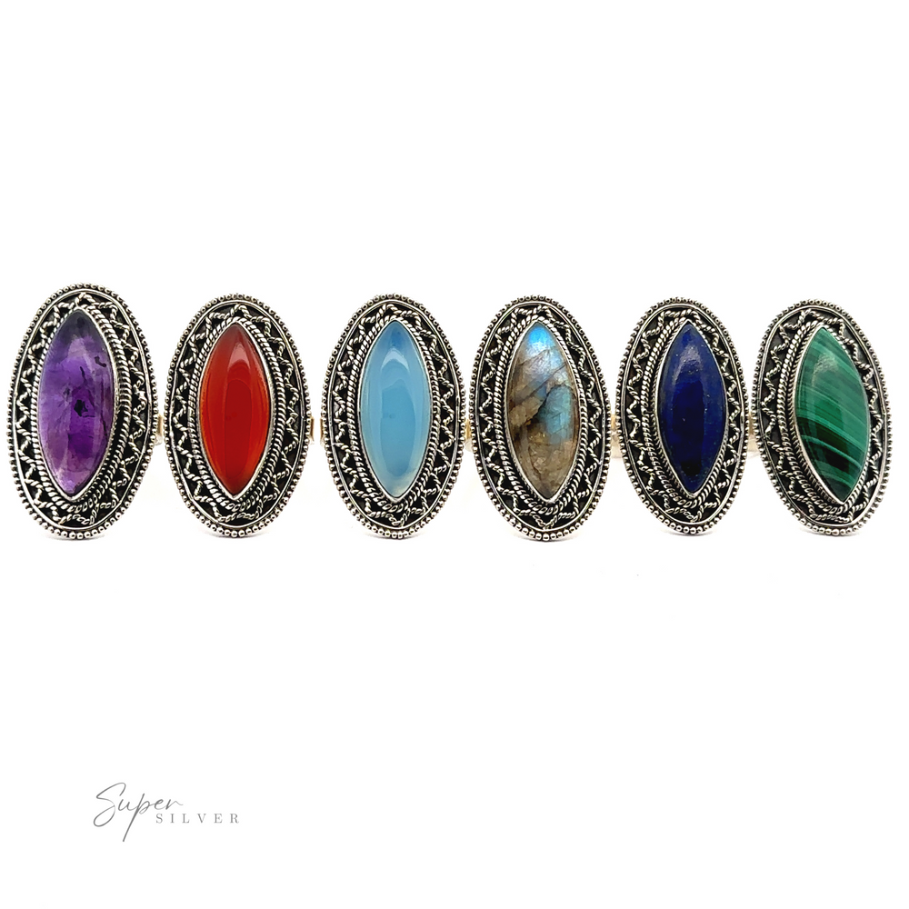 
                  
                    Six Marquise Shaped Gemstone Rings With Vintage Shield Borders with various colored stones in the center, including purple, red, light blue, brown, dark blue, and green, displayed in a row on a plain white background. Each ring boasts a Bohemian twist that adds an eclectic charm to any look.
                  
                