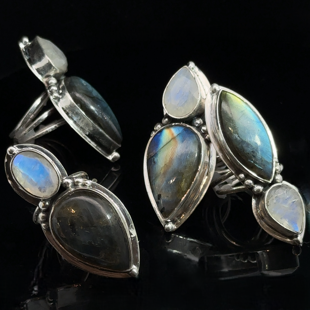 
                  
                    Three **Heavy Labradorite And Moonstone Rings** with large, polished labradorite and moonstone gemstones on a black background make for the perfect statement pieces.
                  
                