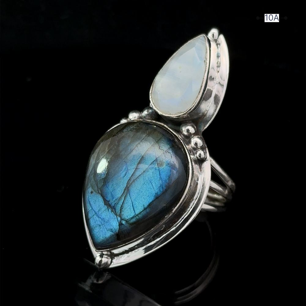 
                  
                    The Heavy Labradorite And Moonstone Ring showcases a dual-stone design, featuring a pear-shaped blue labradorite and a smaller tear-drop shaped moonstone set on a dark background.
                  
                