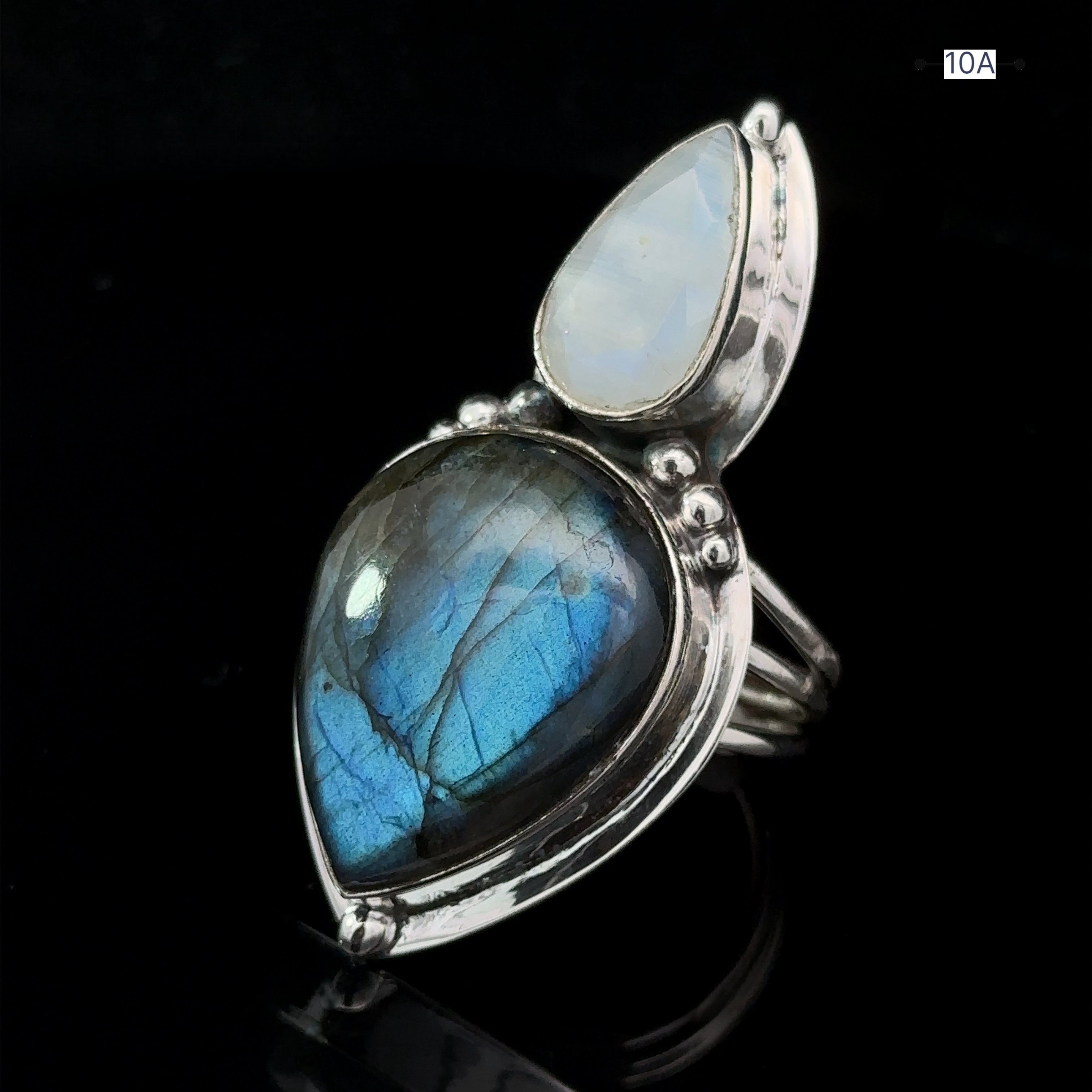 The Heavy Labradorite And Moonstone Ring showcases a dual-stone design, featuring a pear-shaped blue labradorite and a smaller tear-drop shaped moonstone set on a dark background.