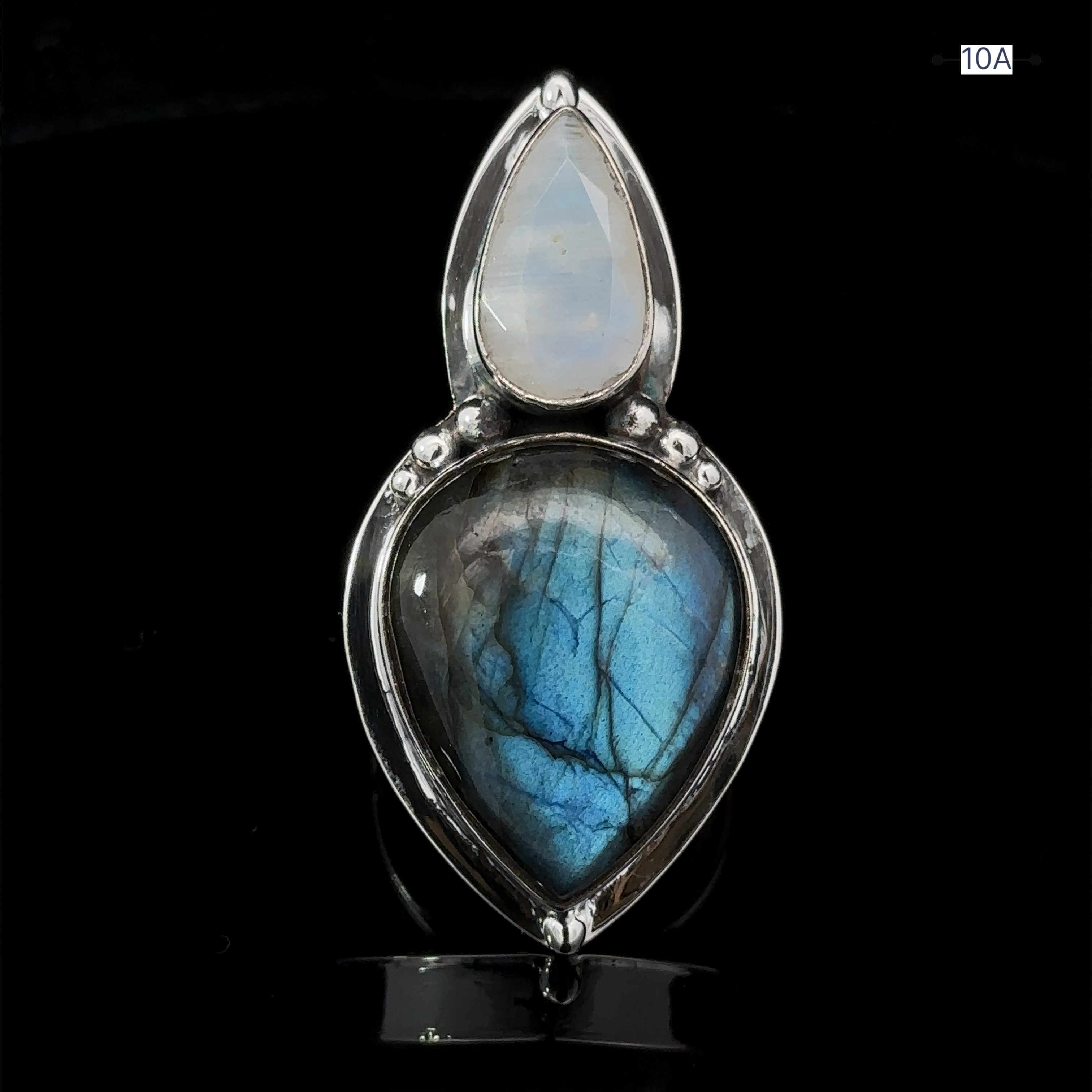 A statement piece named the Heavy Labradorite And Moonstone Ring, featuring a blue gemstone in the shape of a teardrop paired with a smaller teardrop-shaped labradorite, all set against a striking black backdrop.