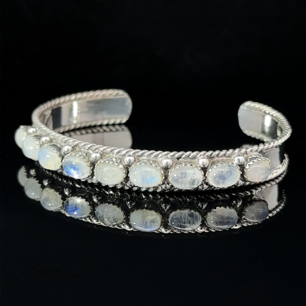 
                  
                    An Oval Moonstone Cuff Bracelet with a row of opalescent stones set along the top, displayed against a black background.
                  
                