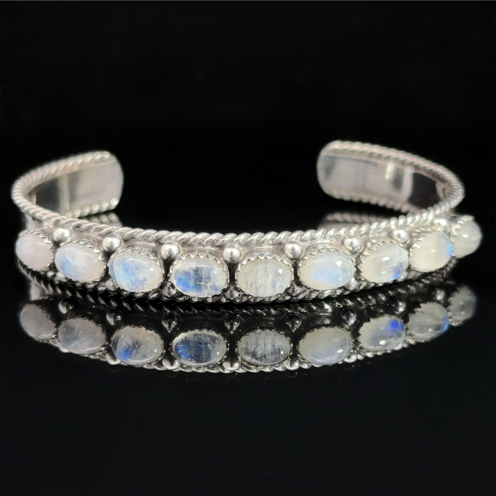 
                  
                    Oval Moonstone Cuff Bracelet: A silver cuff bracelet with oval moonstone gemstones set in a row on a black background, known for its metaphysical properties and emotional healing benefits.
                  
                