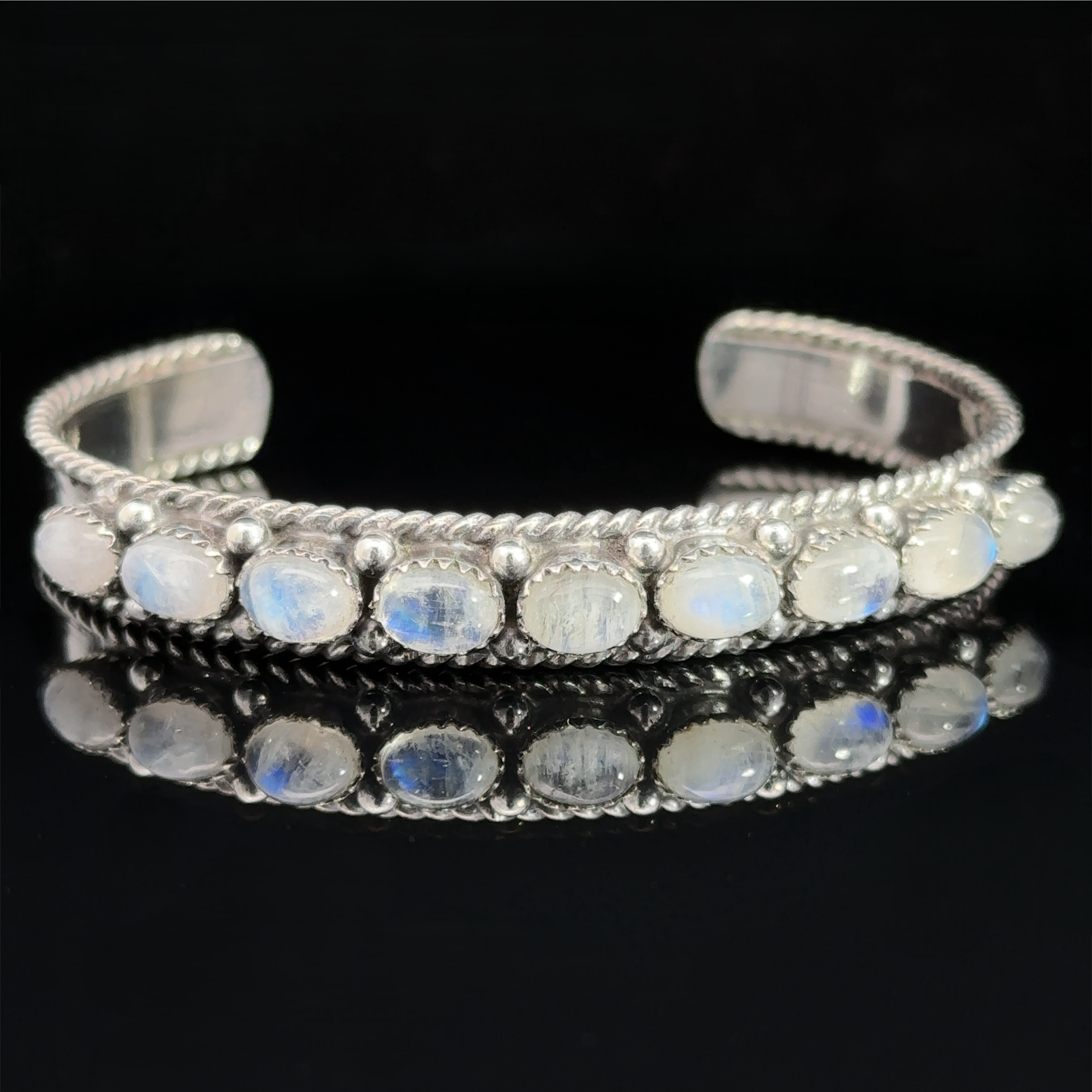 Oval Moonstone Cuff Bracelet: A silver cuff bracelet with oval moonstone gemstones set in a row on a black background, known for its metaphysical properties and emotional healing benefits.