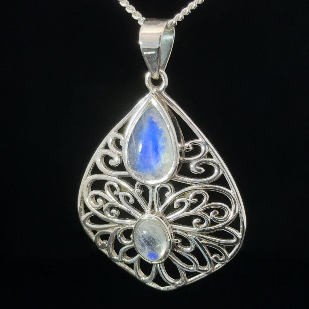 
                  
                    The **Teardrop Filigree Gemstone Pendants** with intricate filigree design featuring two blue gemstones, one teardrop-shaped at the top and an oval one below, hanging from a silver chain against a black background.
                  
                