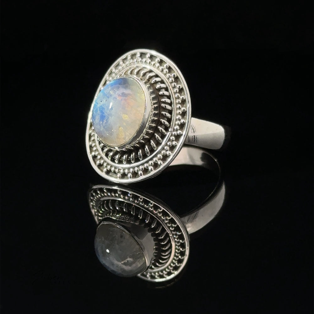 Moonstone ring with a braided disc design set in a detailed bezel, reflecting on a dark surface.