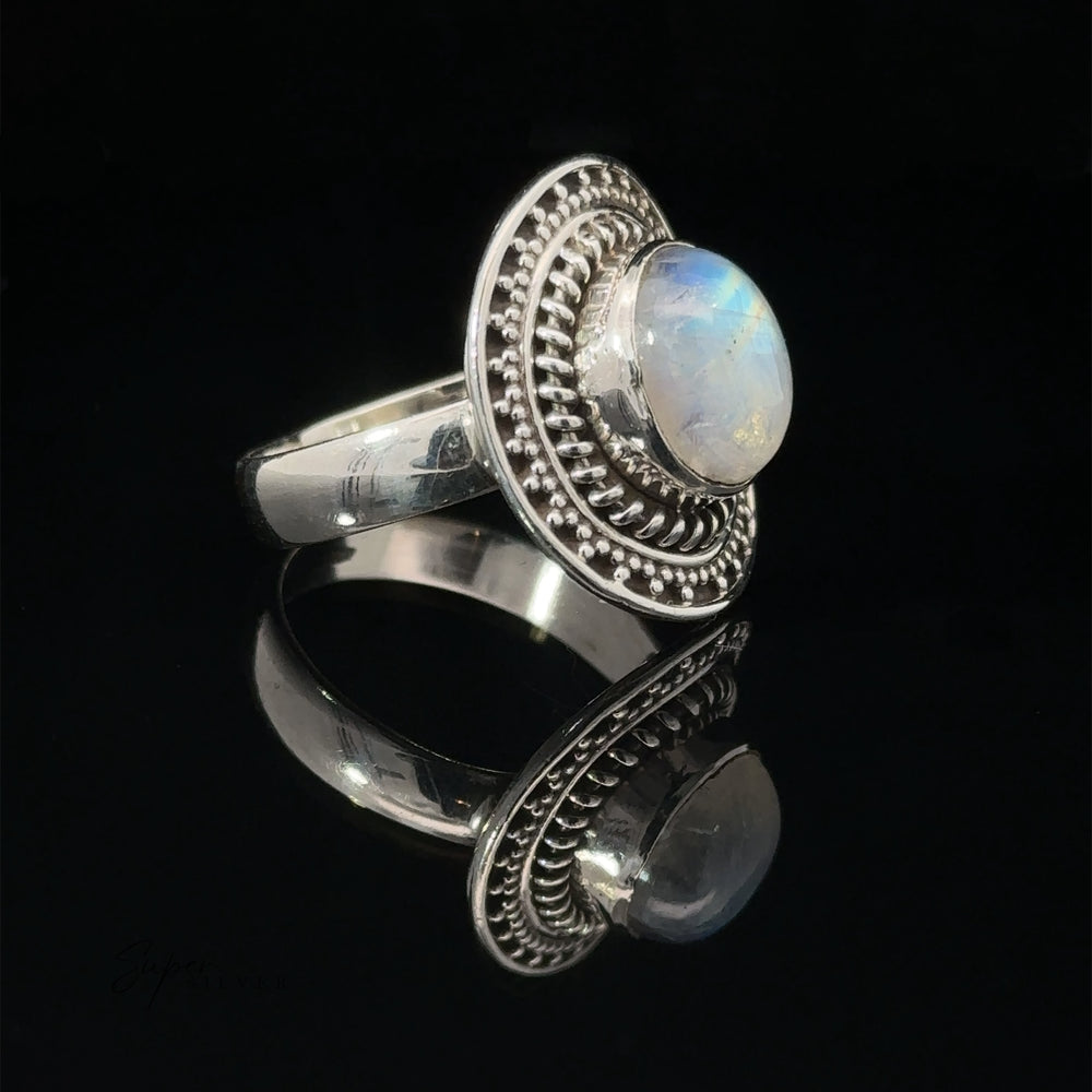 
                  
                    Moonstone Ring With Braided Disc Design, featuring a decorative border and set on a reflective surface.
                  
                