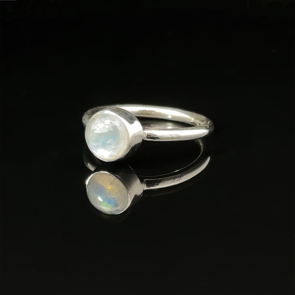 
                  
                    Round Moonstone Ring with a moonstone on a reflective black surface.
                  
                