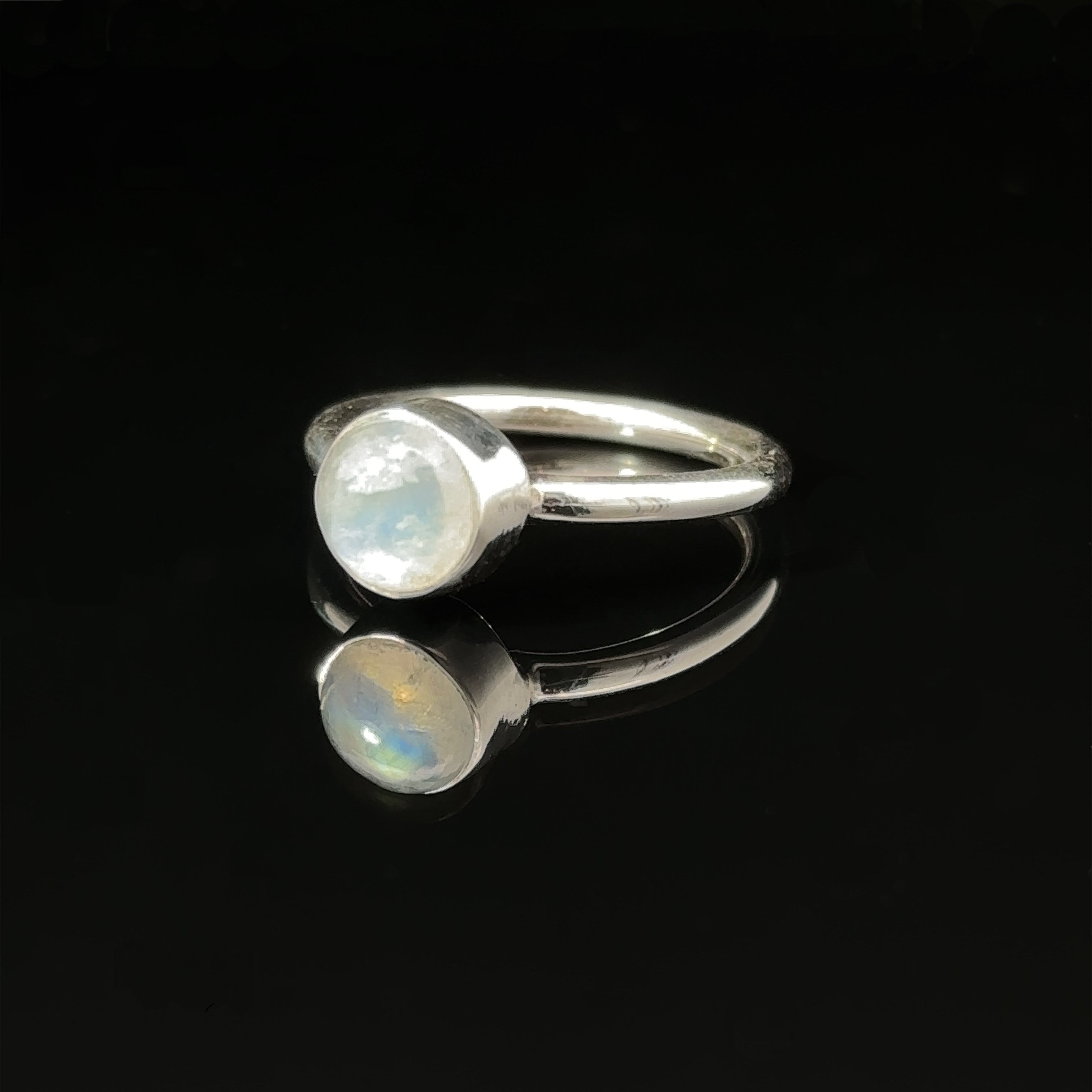 Round Moonstone Ring with a moonstone on a reflective black surface.