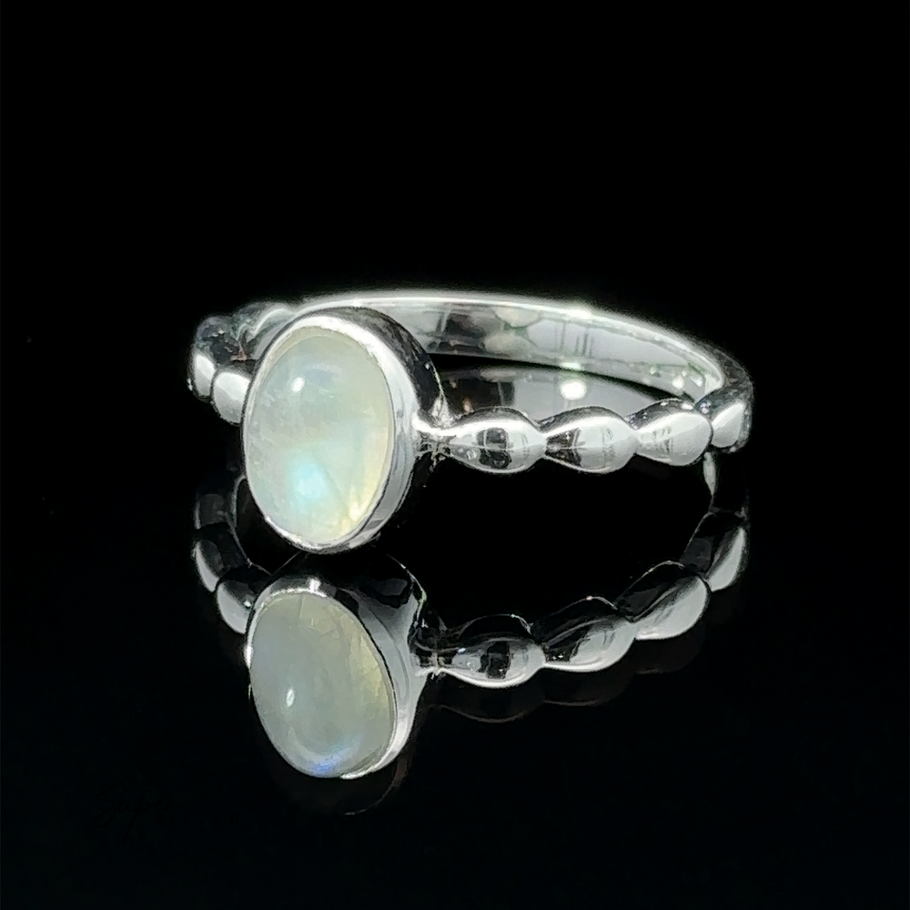 
                  
                    Oval Gemstone Ring with Beaded Band with an oval opal set on a reflective black surface, showcasing its iridescent hues and twisted band design.
                  
                