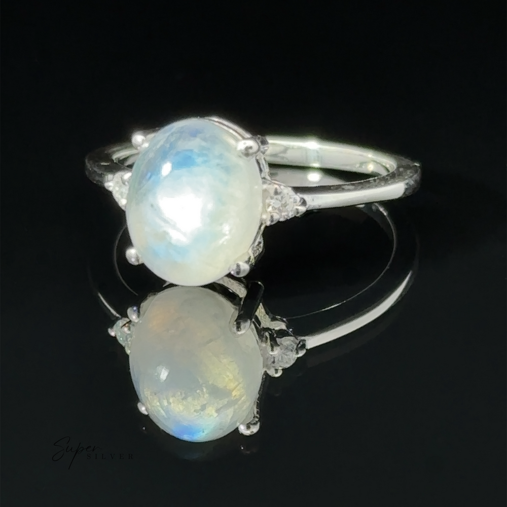 
                  
                    Brilliant Pronged Oval Gemstone Ring with a large opal set in a prong setting between two smaller clear stones, displayed on a reflective surface with a black background.
                  
                