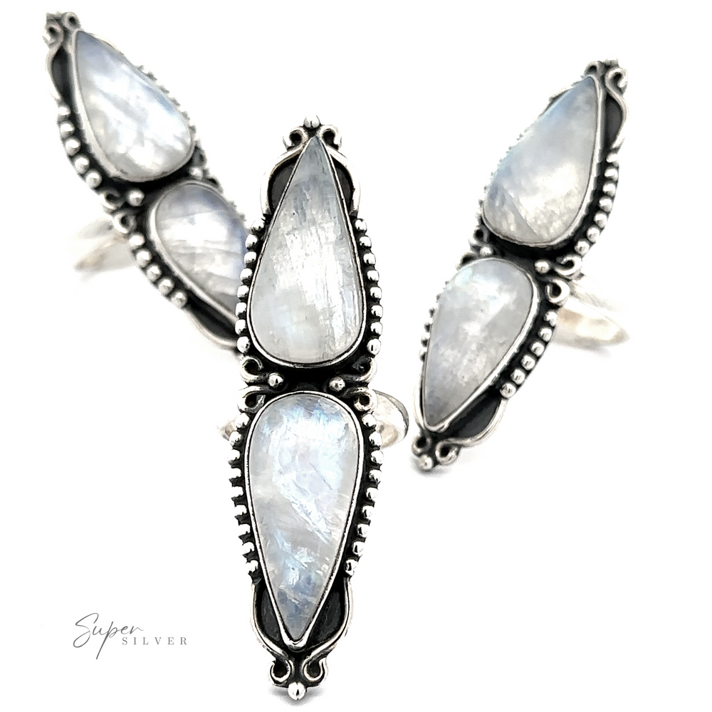 The "Long Double Teardrop Moonstone Ring" by Super Silver is showcased against a white background, featuring four stunning sterling silver rings adorned with teardrop-shaped moonstone gems. Each ring boasts intricate metalwork around the stones, creating a striking statement piece.