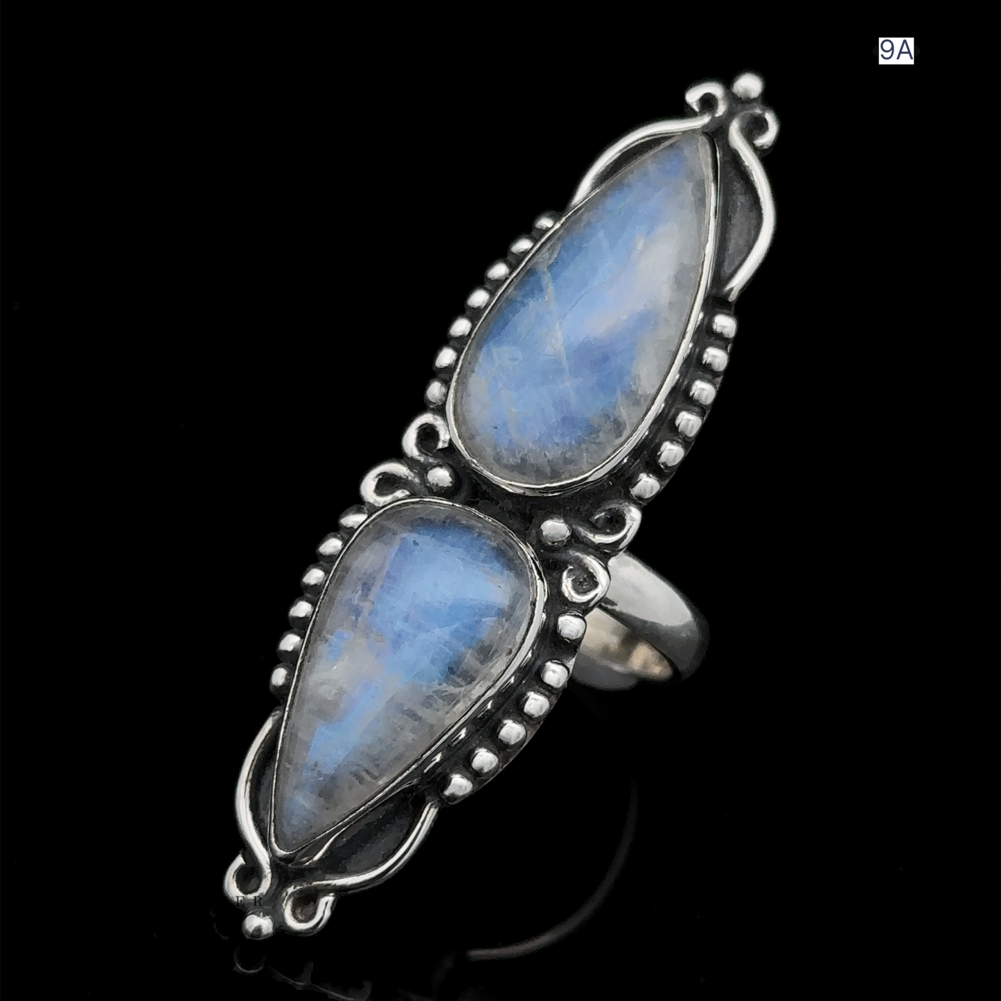 
                  
                    The Long Double Teardrop Moonstone Ring is a sterling silver statement piece showcasing two vertically set, pear-shaped blue moonstone gemstones, adorned with intricate metalwork around each stone and displayed against a black background.
                  
                