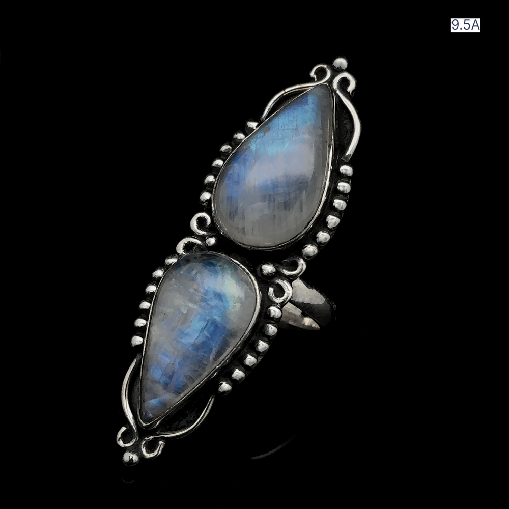 
                  
                    The Long Double Teardrop Moonstone Ring, a stunning sterling silver piece with two teardrop-shaped blue gemstones set vertically and adorned with bead-like details, is elegantly showcased on a black background. This statement ring exudes elegance and sophistication.
                  
                