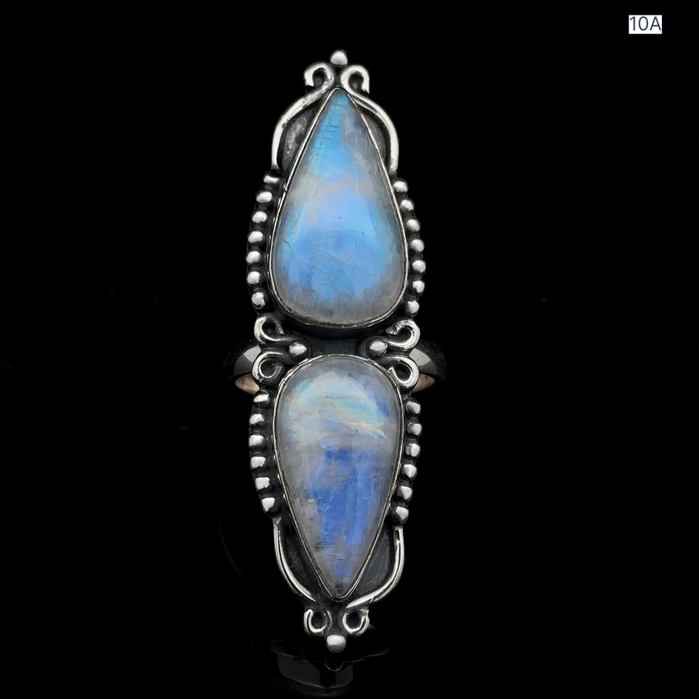 
                  
                    The Long Double Teardrop Moonstone Ring is a sterling silver statement piece showcasing two vertically-aligned, teardrop-shaped blue moonstones with intricate detailing, set against a plain black background.
                  
                