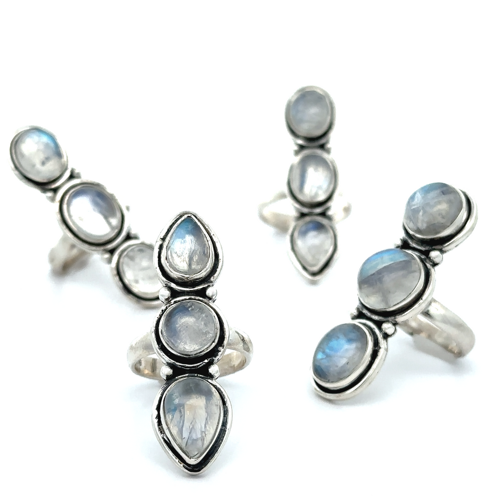 
                  
                    A display of Triple Moonstone Rings in sterling silver showcases large, oval, and teardrop-shaped moonstone settings beautifully arranged on a white background. Each ring radiates goddess energy, shimmering with ethereal beauty.
                  
                