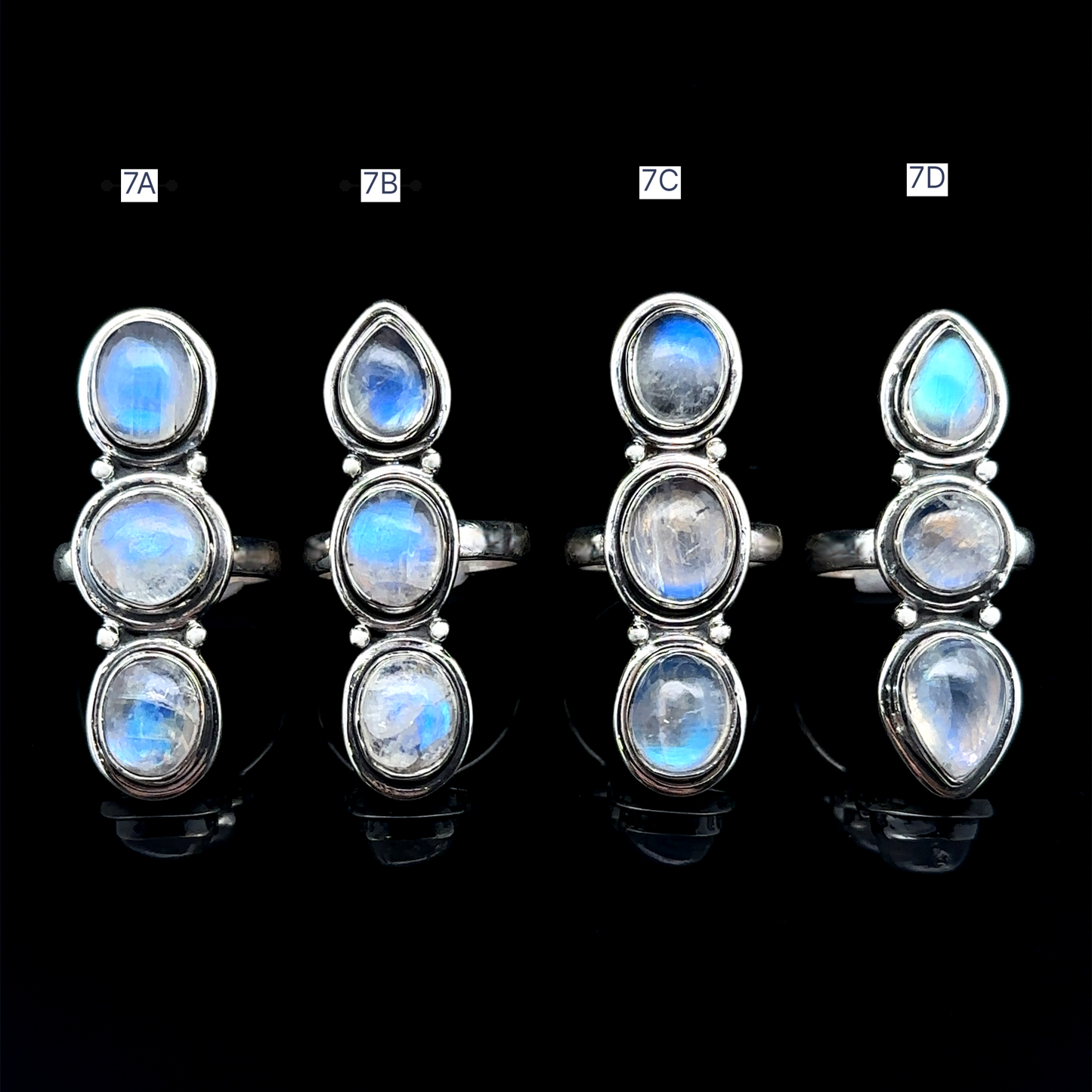 
                  
                    Against a black background, four Triple Moonstone Rings are displayed vertically, each adorned with three oval moonstones. Labeled as 7A, 7B, 7C, and 7D, these sterling silver rings embody the mystical allure of goddess energy.
                  
                