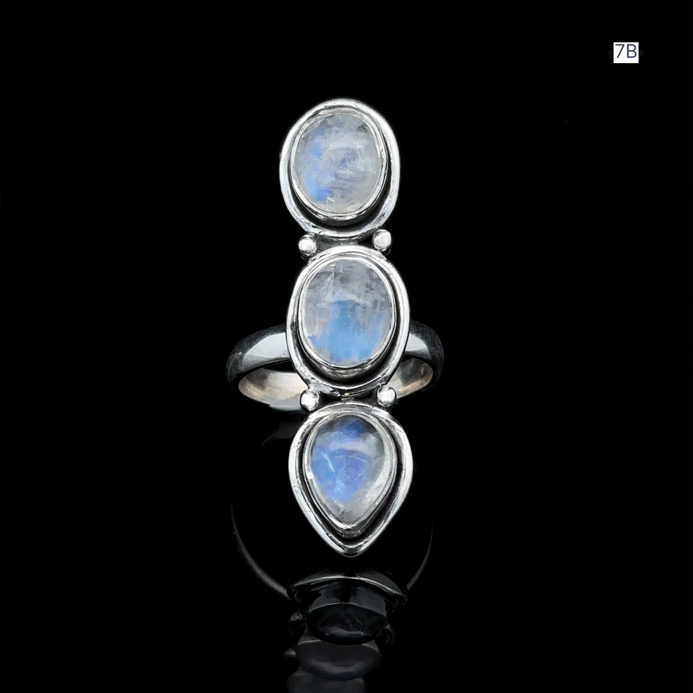 
                  
                    The Triple Moonstone Ring showcases three oval moonstone gems set in sterling silver, exuding goddess energy against a black background.
                  
                