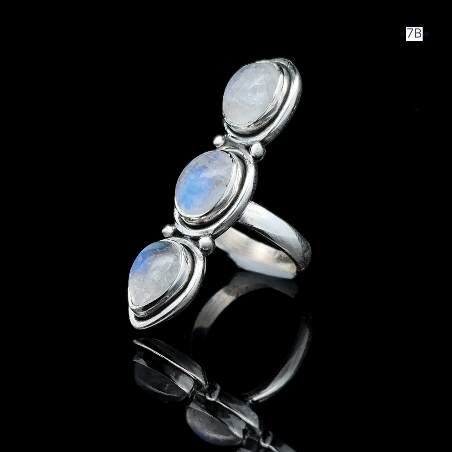 
                  
                    Triple Moonstone Ring showcasing three vertically aligned oval moonstones on a reflective black surface, intricately crafted in sterling silver to evoke goddess energy.
                  
                