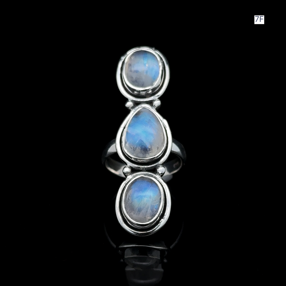 
                  
                    The Triple Moonstone Ring features three oval blue gemstones set vertically against a striking black background, radiating goddess energy.
                  
                