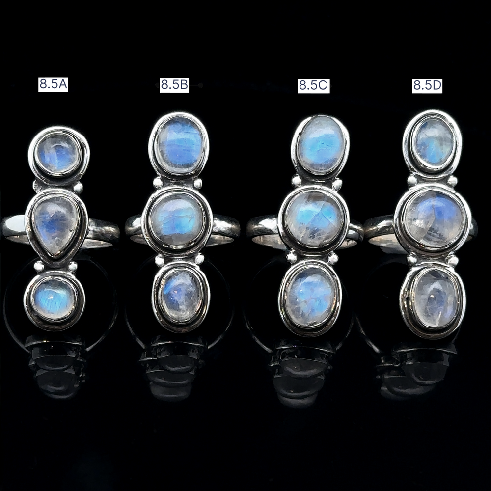 
                  
                    Four Triple Moonstone Rings, labeled 8.5A to 8.5D, displayed in a row on a black background, exuding goddess energy.
                  
                