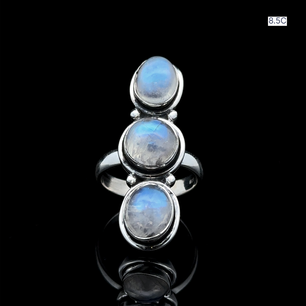 
                  
                    The Triple Moonstone Ring, crafted from sterling silver and featuring three captivating oval moonstone gems, evokes goddess energy as it elegantly rests on a black reflective surface.
                  
                