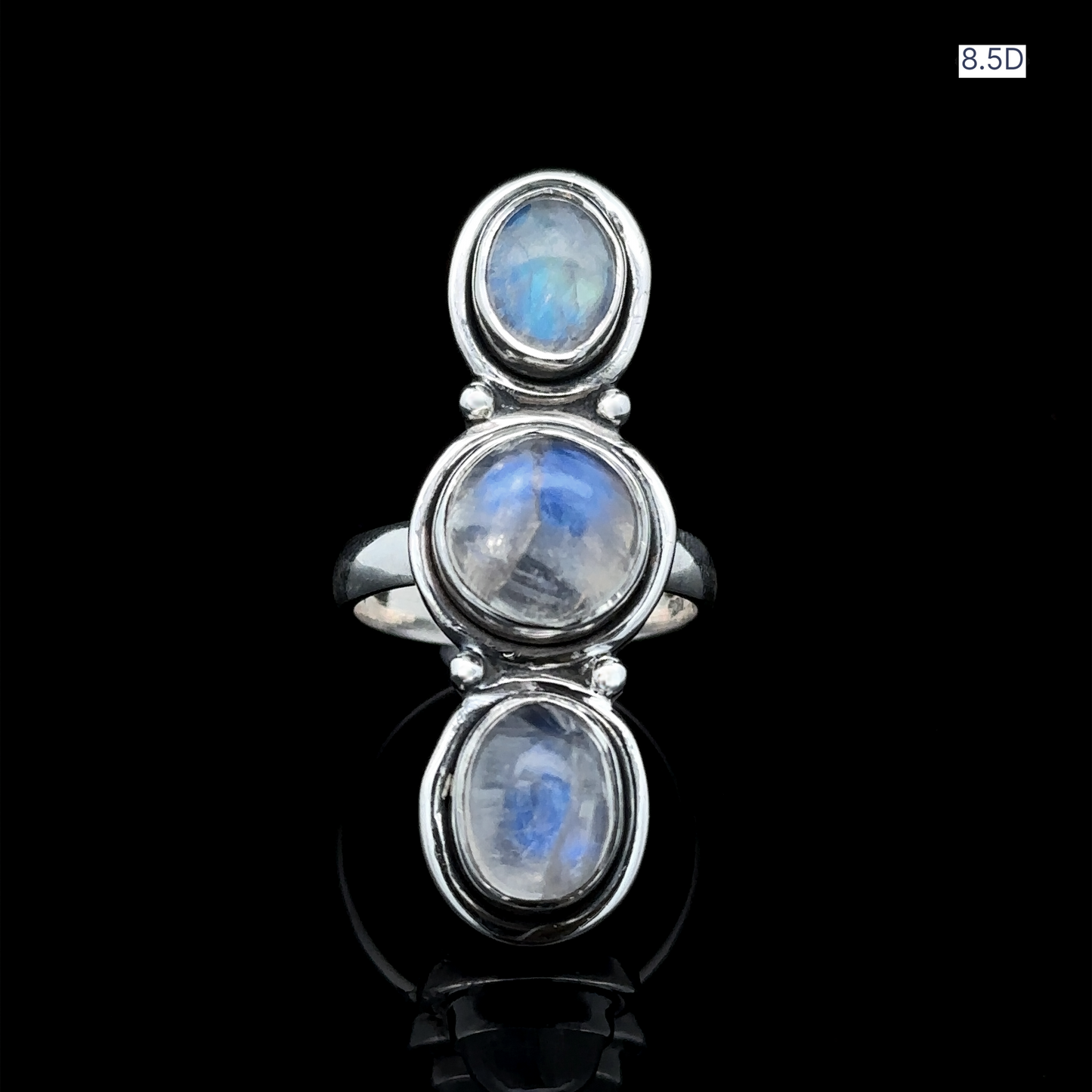 
                  
                    Triple Moonstone Ring featuring three vertically set round stones in sterling silver, embodies goddess energy on a sleek black surface.
                  
                