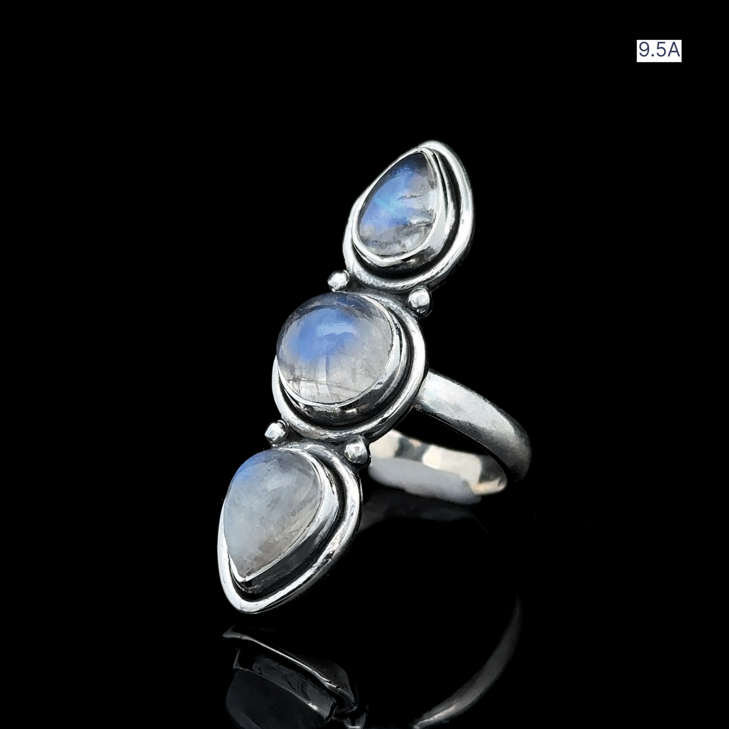 
                  
                    The Triple Moonstone Ring is made from sterling silver and showcases three vertically set teardrop-shaped moonstones against a black background, emanating goddess energy. It is available in size 9.5A.
                  
                