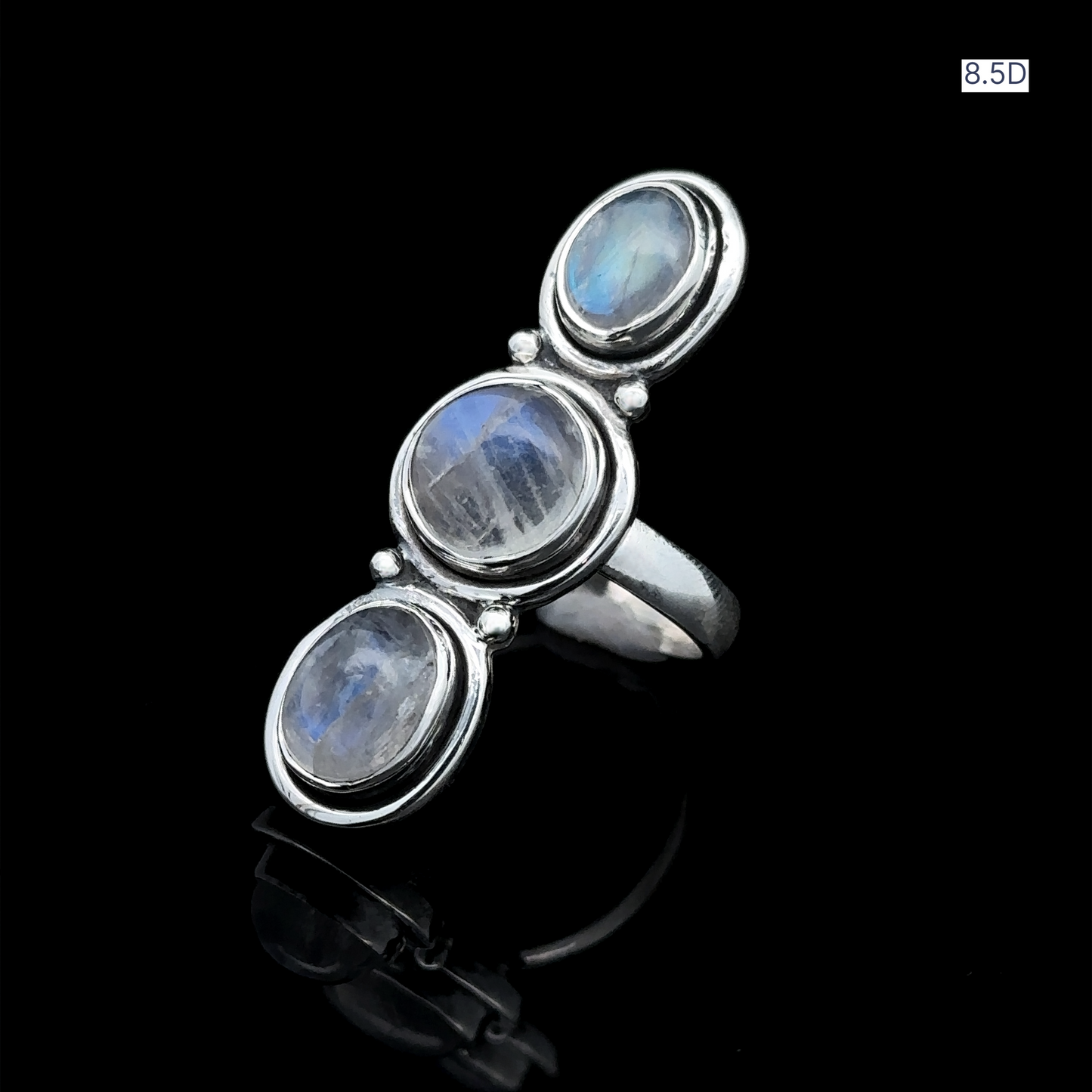 
                  
                    The Triple Moonstone Ring exudes goddess energy with its stunning design, featuring three vertically set oval moonstones in sterling silver, beautifully displayed on a reflective black surface.
                  
                