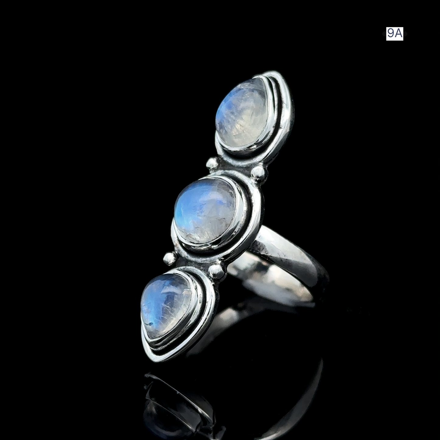 
                  
                    Triple Moonstone Ring crafted from sterling silver and adorned with three round moonstone gems that radiate goddess energy against a black backdrop.
                  
                