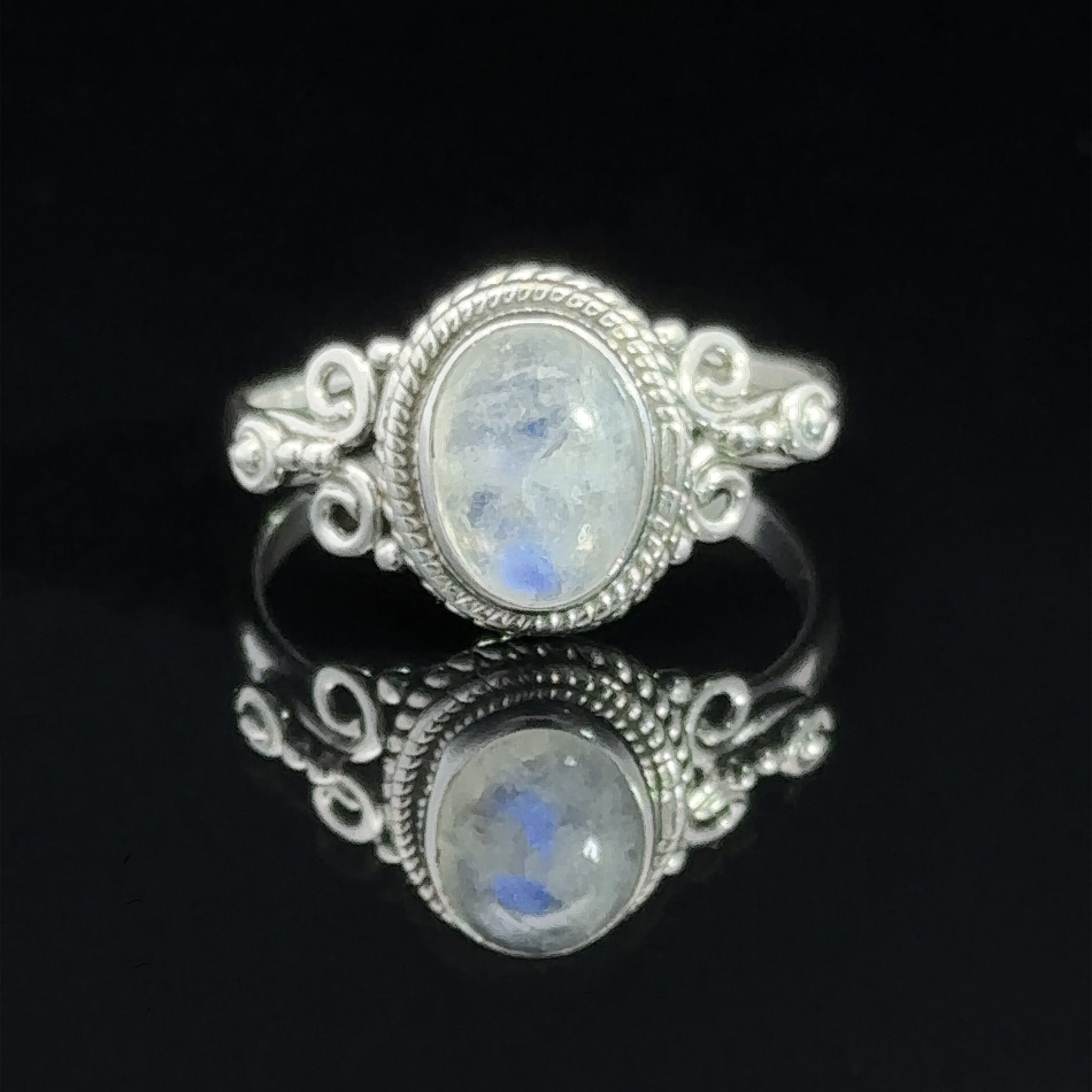 A Natural Oval Gemstone Ring with Intricate Rope and Long Spiral Border, reflected on a glossy surface.
