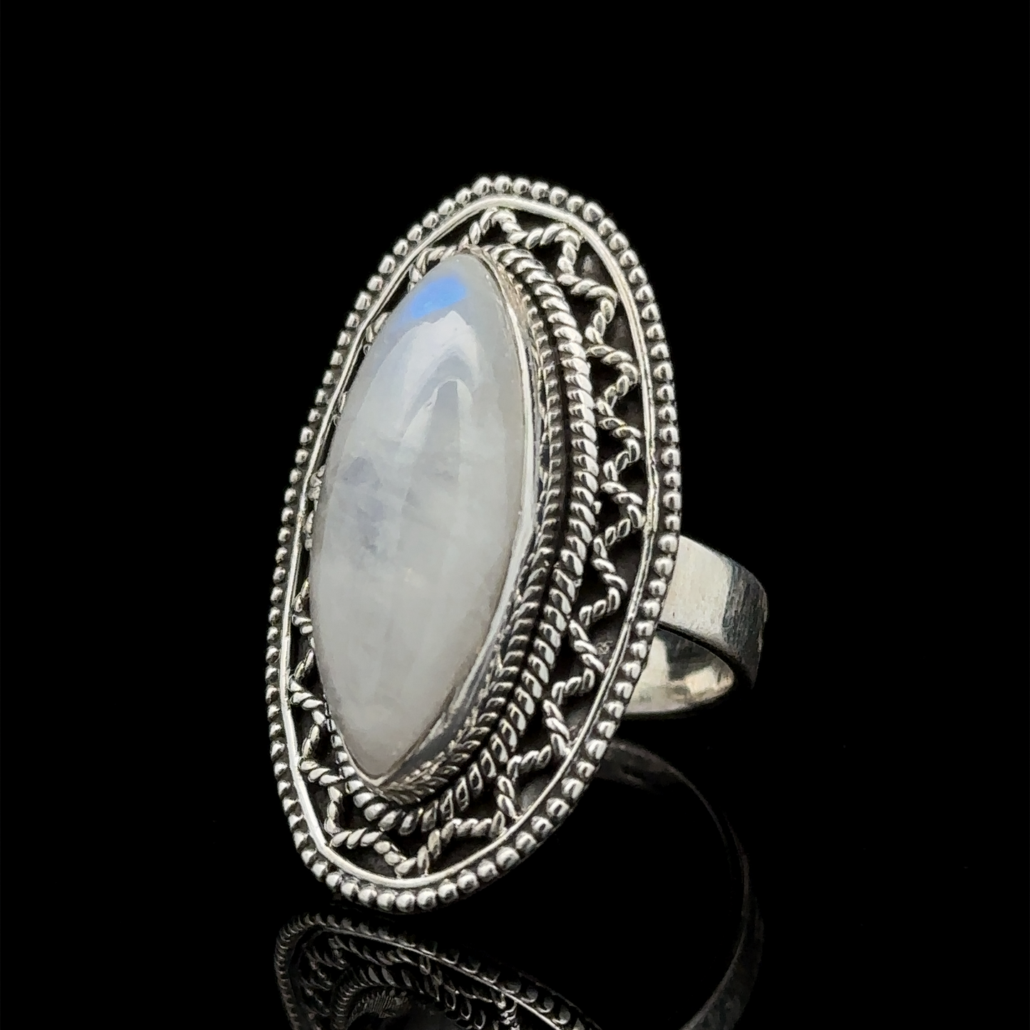 
                  
                    An oval-shaped moonstone set in an intricately designed sterling silver ring with a detailed band and filigree pattern, displayed against a black background, offers a subtle Bohemian twist of the Marquise Shaped Gemstone Ring With Vintage Shield Border.
                  
                